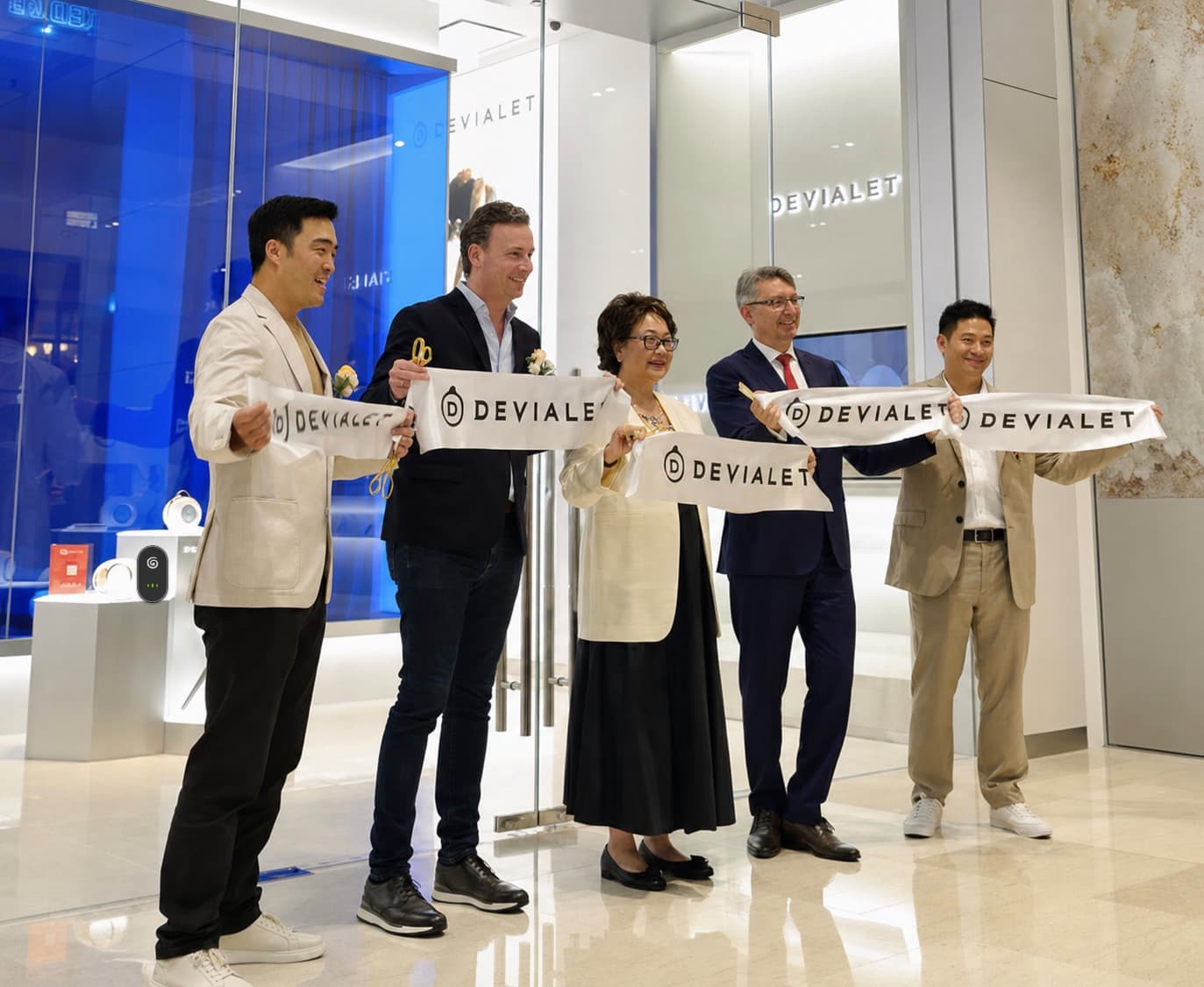 Five people hold a Devialet-branded ribbon at the opening of a Devialet store, with Phantom speakers on display behind them.