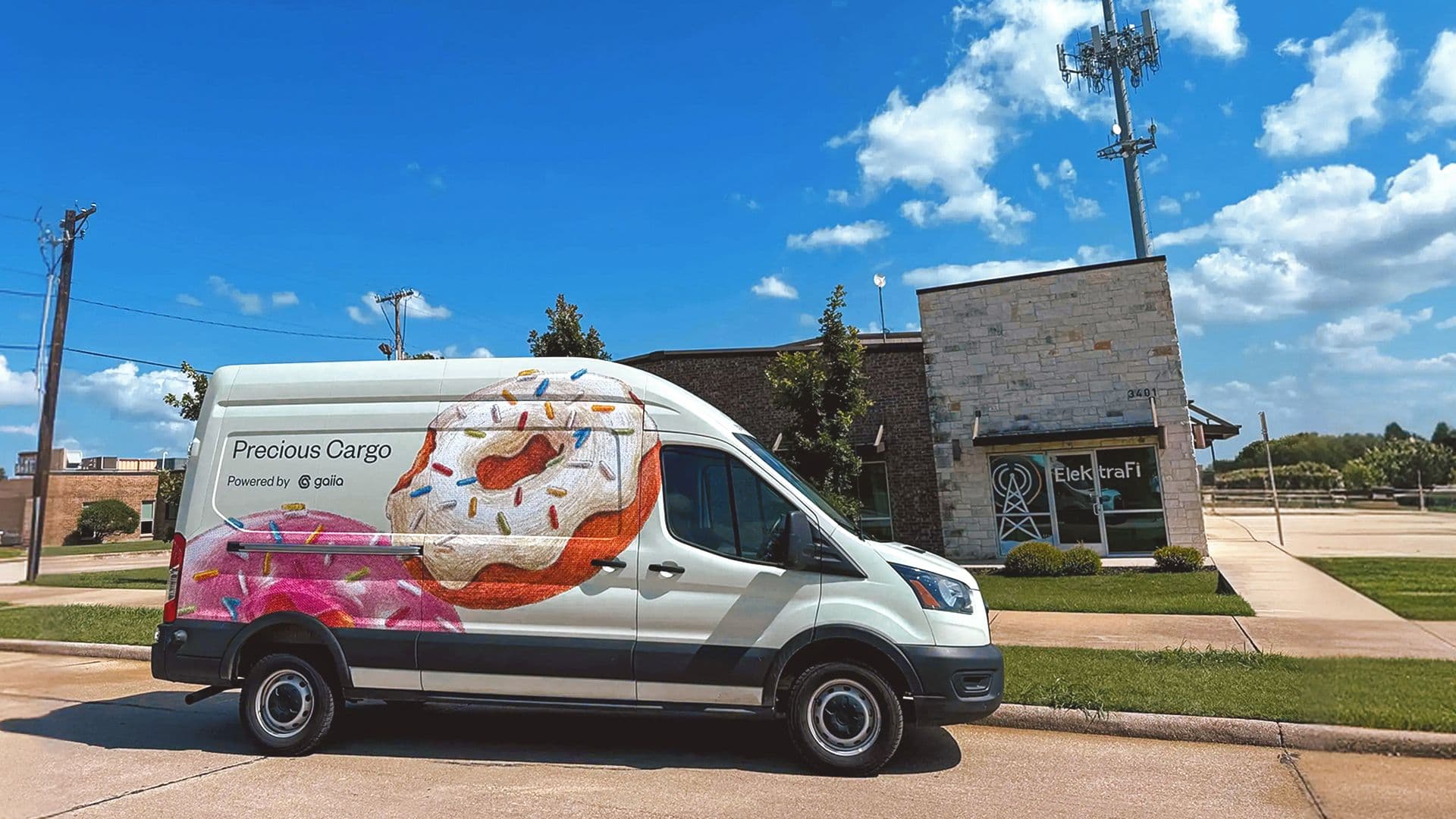 An ElektraFi service van wrapped in a large doughnut illustration, lettered "Precious Cargo — Powered by gaiia", parked outside the ElektraFi office.