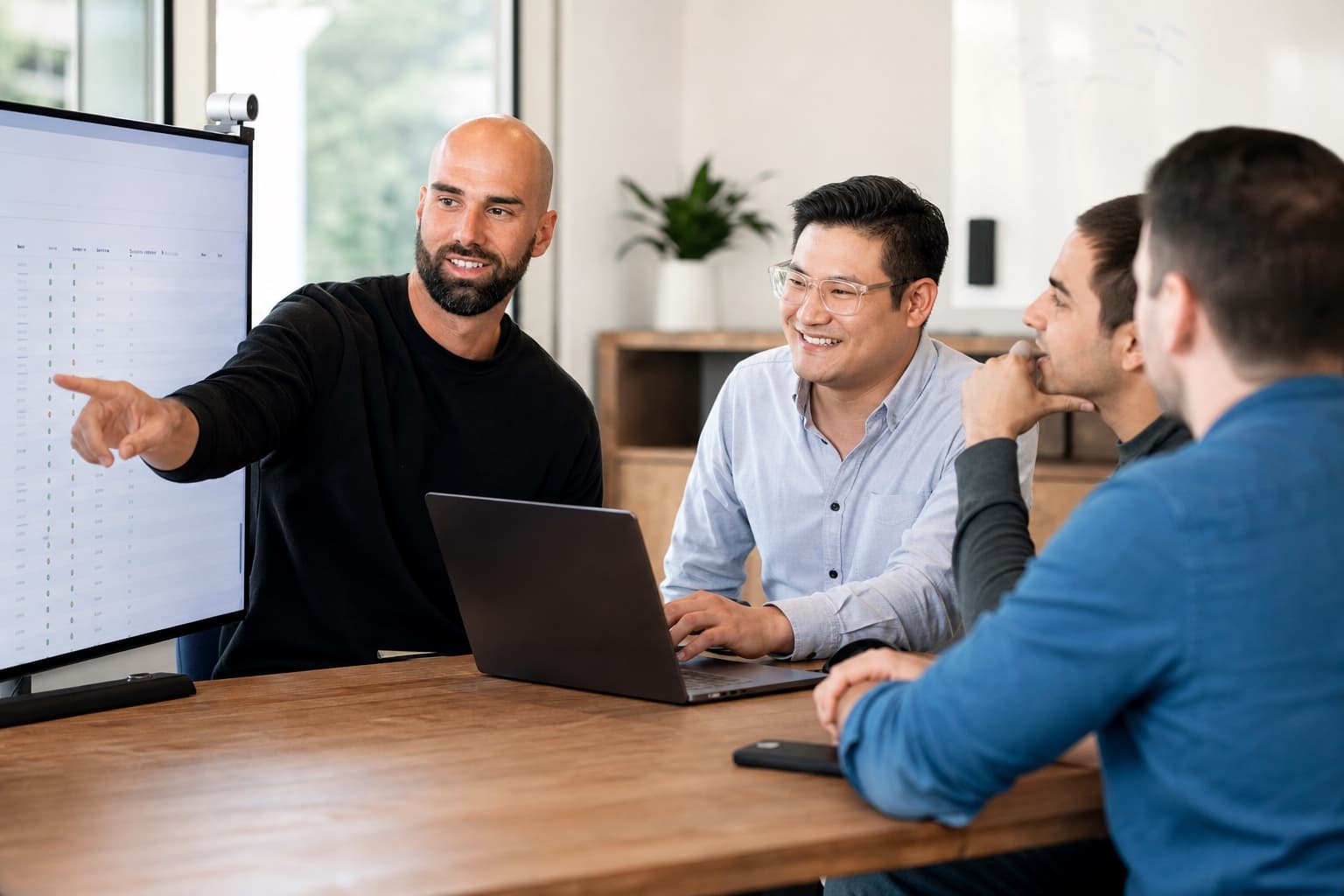 Four people reviewing a dashboard on a conference-room monitor.